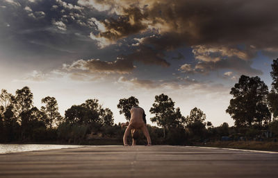 Shirtless man practicing yoga on pier against sky during sunset