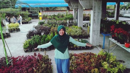 Portrait of smiling young woman standing by potted plants