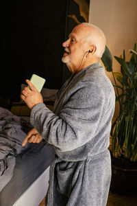 Side view of senior man dancing and listening music in bedroom at home