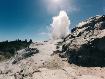Scenic view of geyser erupting on mountain against sky