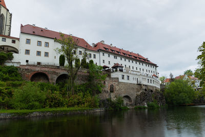 Arch bridge over river by buildings against sky