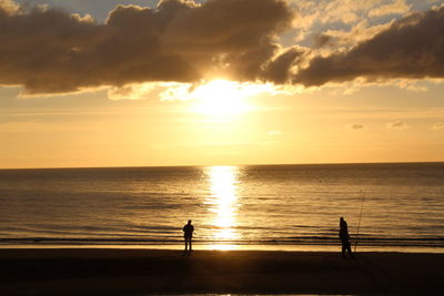 Silhouette people fishing at beach against sky during sunset