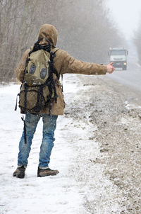 Rear view of man standing on snow by road