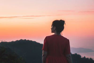 Rear view of woman standing against orange sky