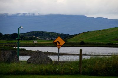 Road sign on field by mountains against sky