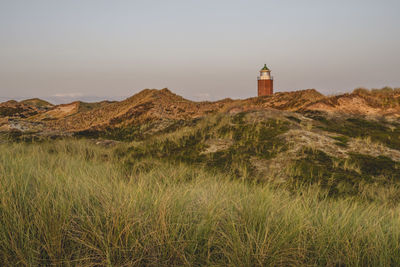 Lighthouse on field by mountain against sky