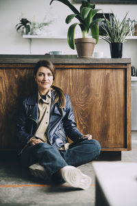 Full length portrait of creative businesswoman sitting against kitchen island in office