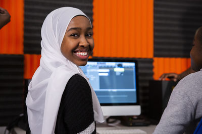 Portrait of smiling girl with hijab sitting in recording studio