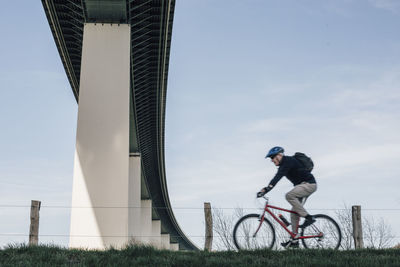 Senior man riding bike, under bridge