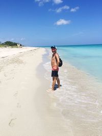 Full length of shirtless man standing on shore against sky at beach during sunny day