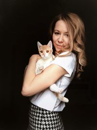 Portrait of woman with cat against black background