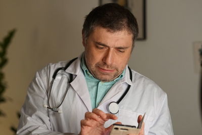 Close-up of mature doctor using phone against wall