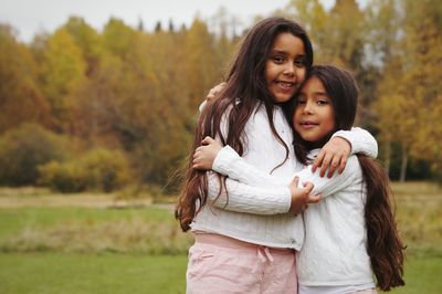 Portrait of smiling sisters standing on field against trees