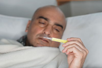 Man checking temperature while lying on bed at home