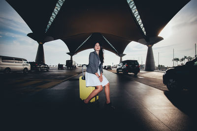 Woman sitting on luggage underneath bridge