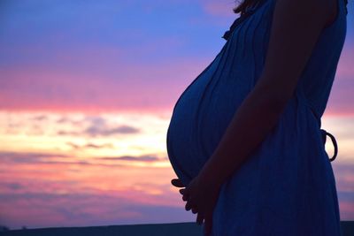 Side view of pregnant woman holding abdomen at sunset