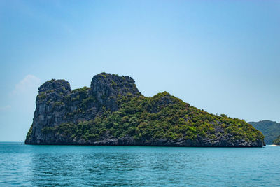 Rock formation in sea against clear blue sky