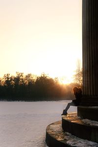 Woman sitting by trees against clear sky during sunset