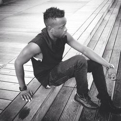 Man looking away while sitting on wooden floor