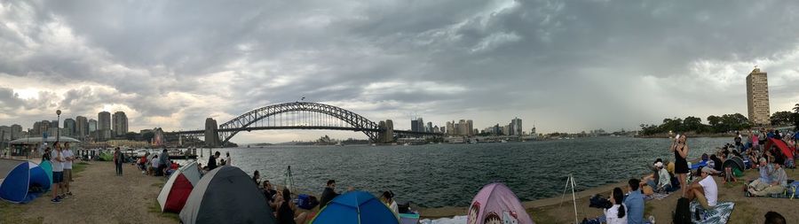 Panoramic view of people at commercial dock against cloudy sky