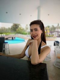 Portrait of woman wearing bikini while sitting at poolside bar counter