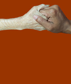 Close-up of man holding hands against orange background