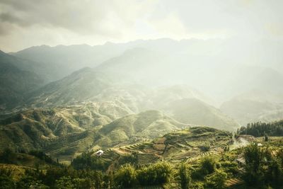 Scenic view of mountains against cloudy sky on sunny day