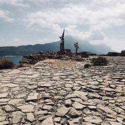 View of cross on rock against cloudy sky