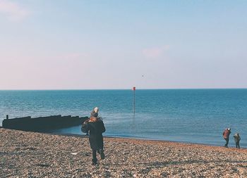 Rear view of men standing on beach against clear sky