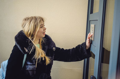 Young woman using intercom on door