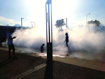 People standing by smoke against sky