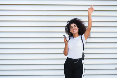 Full length of a smiling young woman standing against wall