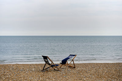 Empty chairs on beach against sky