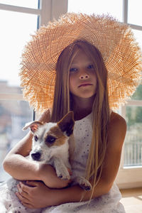 Girl in a white dress and a straw hat sitting on the windowsill with a dog