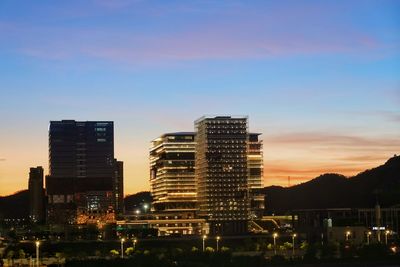 Illuminated buildings in city against sky during sunset