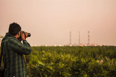 Man photographing through camera while standing on field during sunset