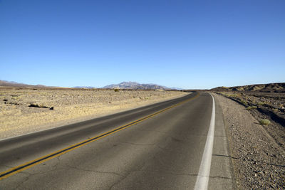 Road leading towards landscape against clear blue sky