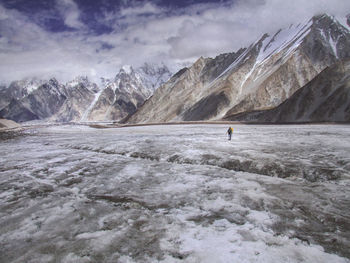 Rear view of man walking on snow covered landscape against cloudy sky