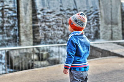 Boy wearing warm clothing standing against waterfall