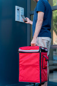 Midsection of delivery person holding parcel bag standing outdoors