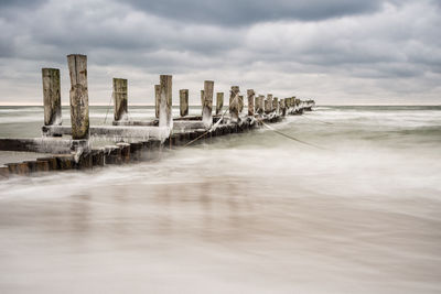 Broken pier on sea against cloudy sky