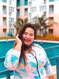 Portrait of smiling young woman standing against swimming pool