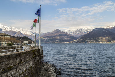 The port of colico with the waving flags of italy and europe with the snow capped alps 