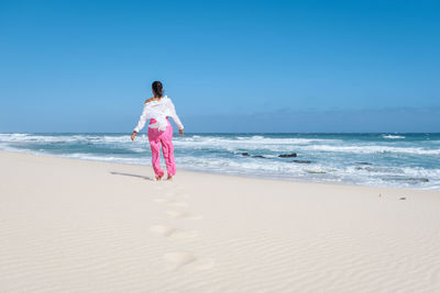 Rear view of woman standing at beach against clear sky