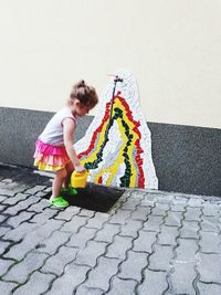 Girl holding umbrella on footpath against wall