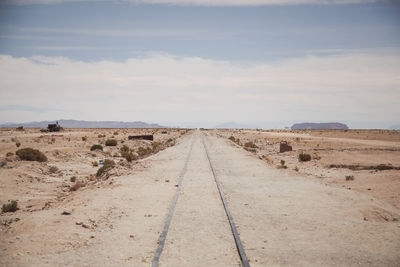 Railroad track in desert against cloudy sky