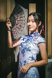 Portrait of young woman with arms raised standing against wall