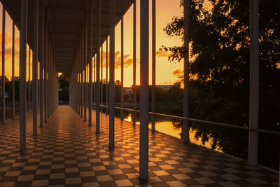 Illuminated footpath amidst buildings against sky during sunset