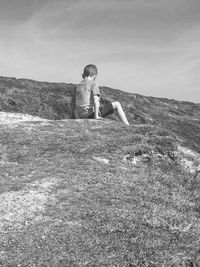 Boy sitting on landscape against sky