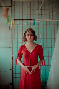 Portrait of young woman in red dress standing at home